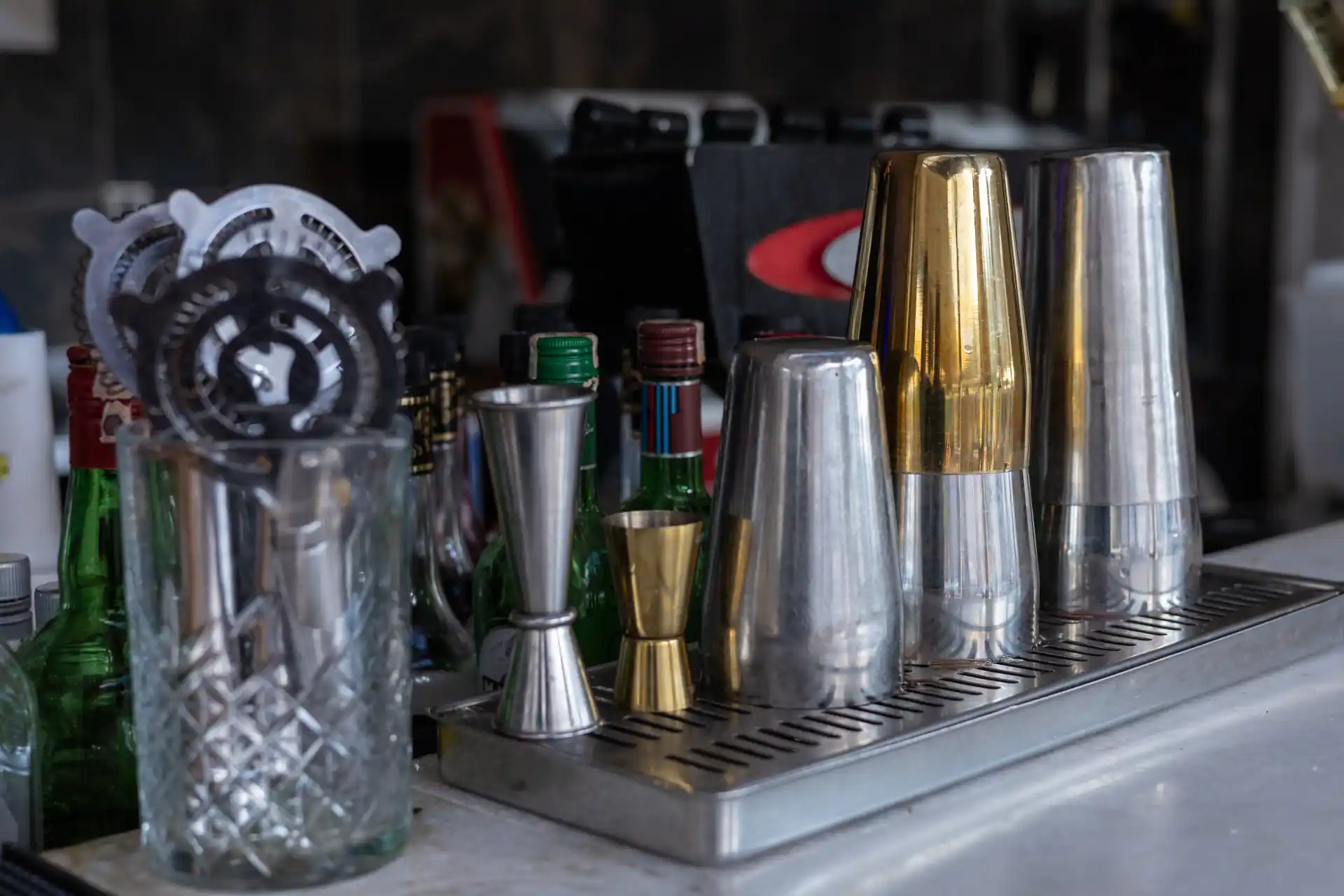 Professionelle Bar-Einrichtung mit Cocktailshakern aus Edelstahl und Messing, Barmaß, Strainer und Flaschen.